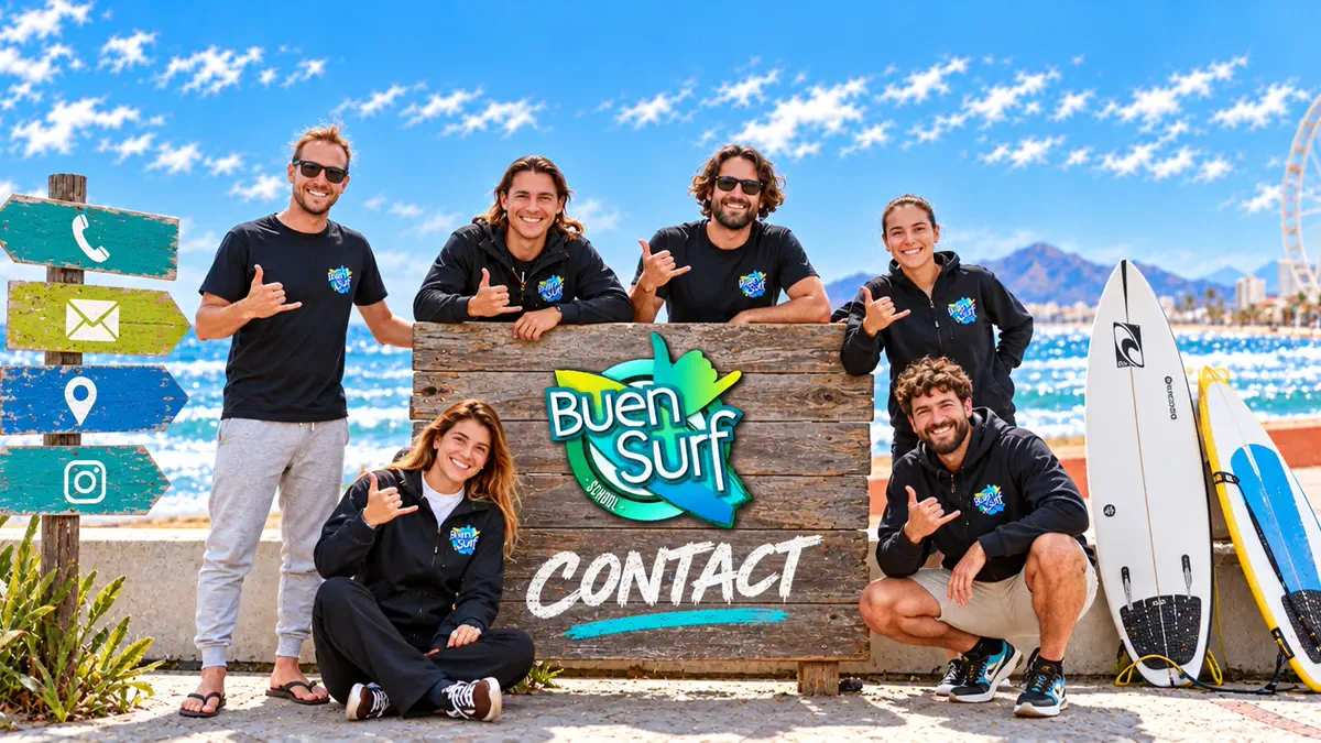 The Buen Surf School team around a wooden sign with the school logo, boards leaning beside them and the sea behind