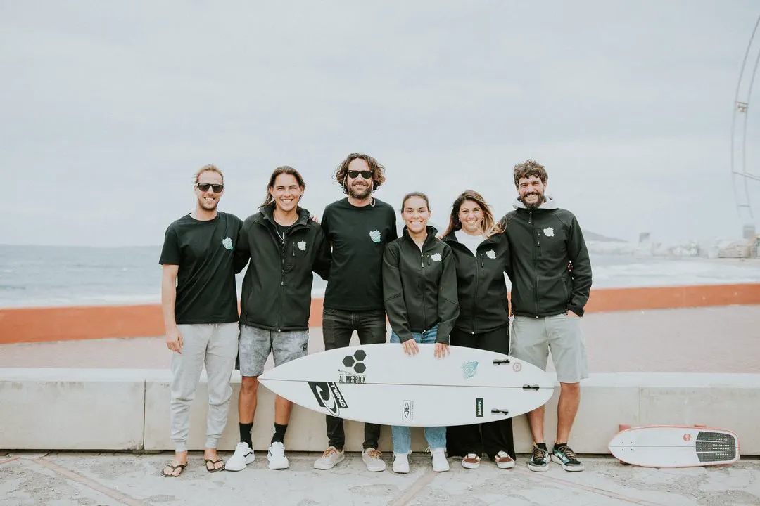 The Buen Surf School team on the seafront promenade, a surfboard standing between them