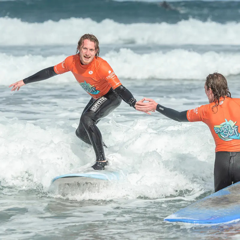 A student standing on the board for the first time, the instructor letting go of their hand